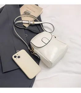 Close-up of small white leather crossbody bag showing U-shaped stitching and compact size