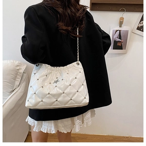 Close-up of white quilted chain bag with star metal clasp and studs on a model