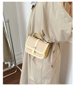 Detail of beige woven crossbody bag with yellow leather trim and metal buckle on coat