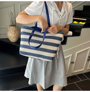 Borsa tote intrecciata a righe bianche e blu con manici scuri indossata da una modella