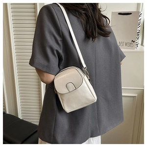 Detail of cream PU leather crossbody bag with gold hardware worn over a grey blazer