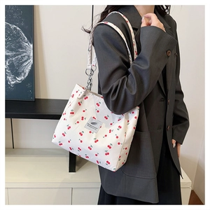 Close-up of stylish cherry print tote bag with metal chain detail on model's shoulder