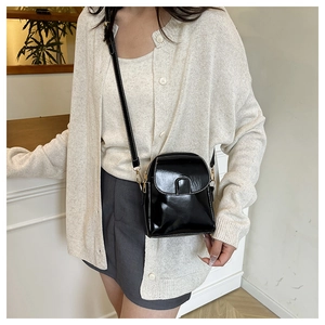 Detail of a shiny black patent leather crossbody bag with golden metal hardware