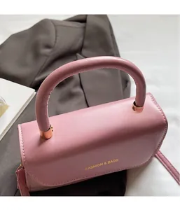 Détail du sac à main en cuir rose montrant l'anse courbée et le logo doré gravé