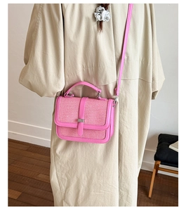 Pink textured fabric handbag with silver clasp carried by model in a cozy interior
