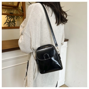 Model wearing a black glossy PU leather vertical crossbody phone bag with gold hardware