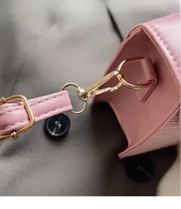 Gros plan du fermoir mousqueton doré et des surpiqûres sur la sangle de sac rose en cuir