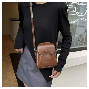 Brown vintage leather crossbody phone bag with contrast stitching on a model in urban setting