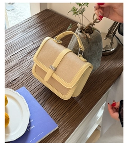 Detail view of woven straw crossbody bag with leather trim and gold buckle on a wooden table