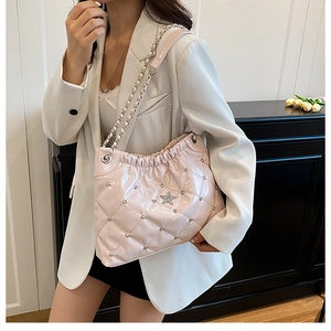 Pink quilted leather bucket bag with silver studs and star emblem worn with a white suit