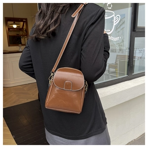 On-body view of a small brown leather crossbody bag with contrast stitching and magnetic flap