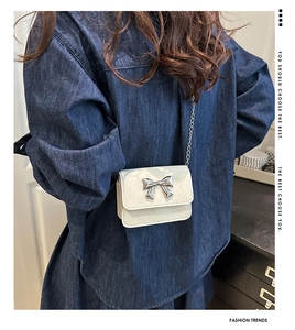 Detail of white mini crossbody bag featuring a silver bow and metallic chain strap