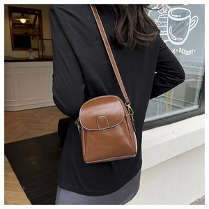 Brown oil wax leather mini crossbody phone bag shown being worn in a stylish cafe setting