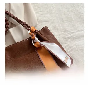 Detail of brown litchi grain leather bucket bag with woven strap and silk scarf