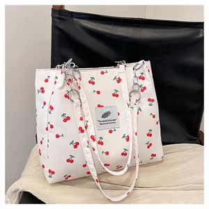 Detail of cherry print tote bag with silver chain and fabric strap on beige surface
