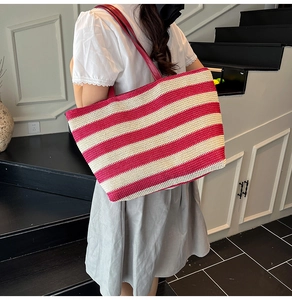 Close-up of a large striped straw tote bag with red leather handles for summer wear