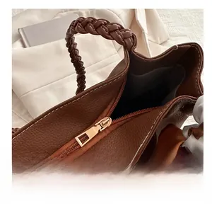 Close-up of brown pebbled leather bag featuring a smooth gold zipper and woven handle