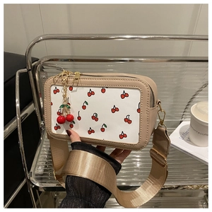 Stylish beige cherry print crossbody bag with wide strap and cherry pendant detail.