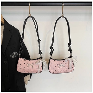 Detail of pink quilted shoulder bag with black trim and elegant pearl bow pendant
