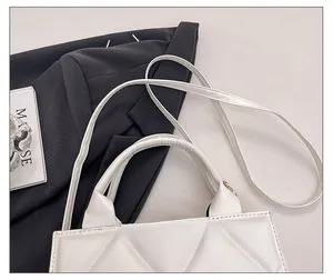 Détail de la bandoulière réglable et de la texture matelassée du sac blanc sur un blazer noir