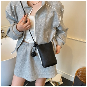 Detail of minimalist black pebbled leather crossbody phone bag with woven ball charm detail