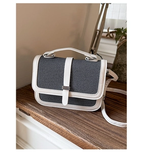 Detailed view of canvas crossbody bag with white leather trim on a vintage wooden table