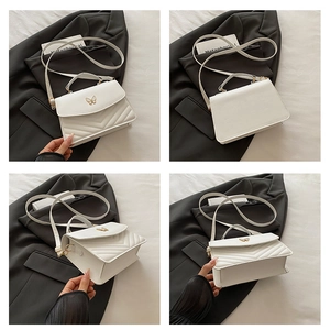 Detail view of white leather crossbody bag featuring gold bow buckle and V-quilted texture