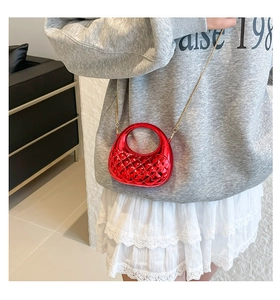 Close-up of a glossy red acrylic clutch with diamond quilting and gold chain strap