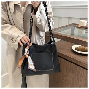 Detail of black pebbled leather tote bag with braided handle and decorative silk scarf