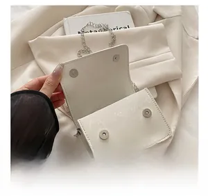 Detail showing dual silver magnetic closures and chain strap on a white mini crossbody bag