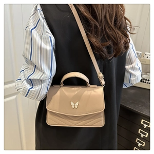 Detail view of a beige quilted crossbody bag featuring a decorative butterfly metal clasp