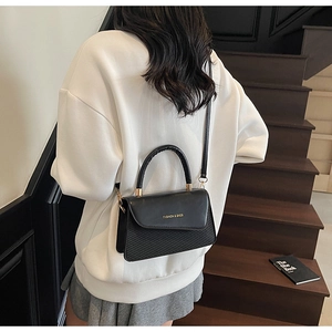 Détail du sac bandoulière noir avec textures contrastées, poignée dorée et lettrage