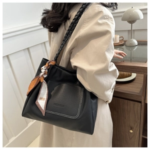 Detail of black pebbled leather tote bag featuring contrast stitching and woven shoulder strap