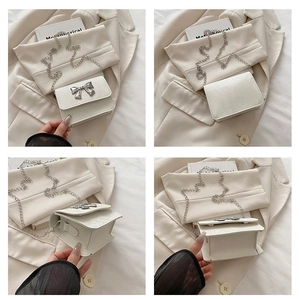 Detail view of mini white chain bag with silver bow buckle and faux snake texture