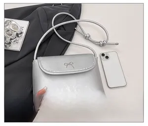 Detail shot of a silver bow-knot crossbody bag showing its compact size next to a phone