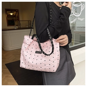 Pink quilted tote bag with black bows and woven strap worn by a model in a cafe