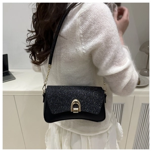 Close-up of black sequined shoulder bag with gold horseshoe buckle on white sweater