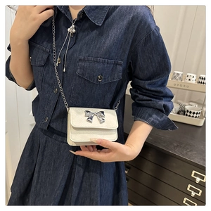 Close-up of cream textured leather mini bag with silver bow buckle on denim outfit
