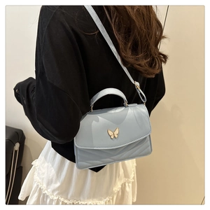 Detail of light blue crossbody bag with gold butterfly clasp and V-quilted texture