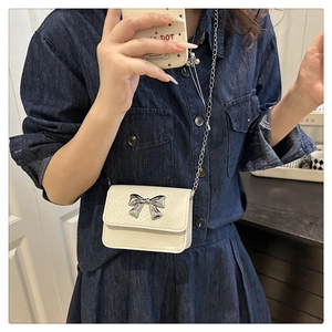 Detail of a white crossbody mini bag with silver bow hardware and thin metal chain strap