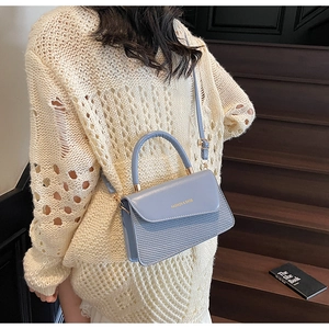 Détail du sac à rabat bleu clair avec texture tissée et lettrage doré de mode