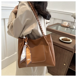Brown leather tote bag featuring a woven strap and decorative scarf in a lifestyle setting