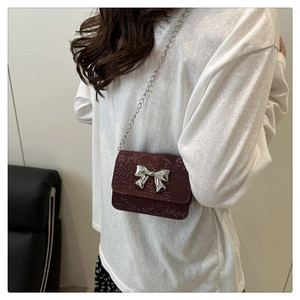 Detail of burgundy snakeskin crossbody bag with silver bow buckle and chain strap