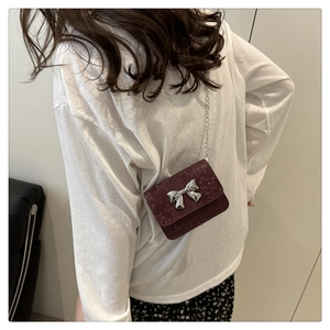 Detail of wine red mini crossbody bag with silver bow ornament and metallic chain strap