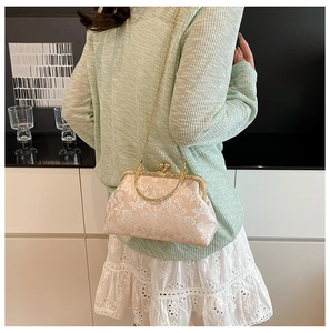 Détail d'une pochette rose clair avec broderie florale blanche et poignée en métal doré