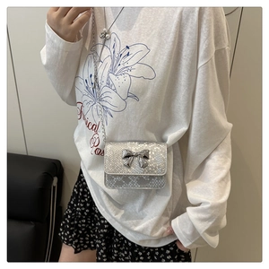 Detail showing snake-patterned mini crossbody bag with a silver metal bow accent