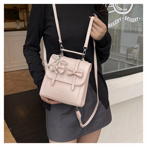 Pink bow square bag with pearl charm and fashion logo shown in a street scene