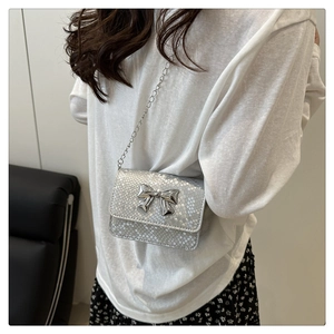 Mini silver snakeskin crossbody bag with metallic bow detail and chain strap worn by model