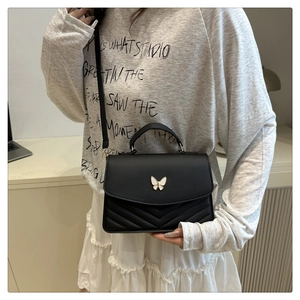 Detail shot of a black crossbody bag with V-shaped quilting and a white butterfly buckle