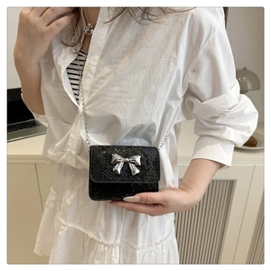 Detailed view of black snake-pattern leather handbag with silver bow buckle and chain